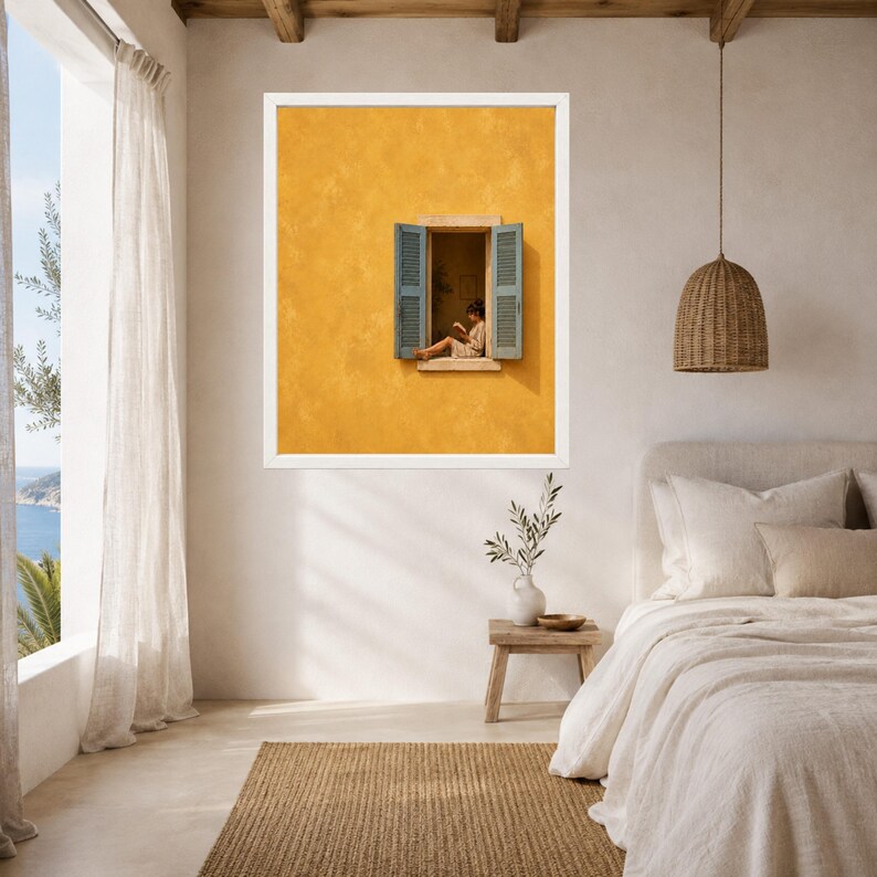 Puede incluir: Una l&aacute;mina de arte enmarcada que muestra una pared de color amarillo mostaza con textura y una ventana abierta. La ventana tiene contraventanas azules y muestra a una persona sentada en el alf&eacute;izar leyendo un libro. Marco de color blanco.