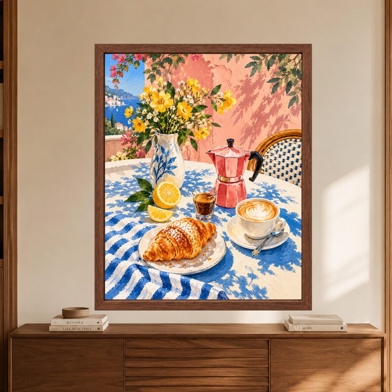 May include: A framed painting depicting a breakfast scene on a table with a blue and white striped tablecloth. The scene includes a croissant on a plate, a cup of latte, a small glass of espresso, a pink moka pot, a vase of yellow flowers, and a lemon.