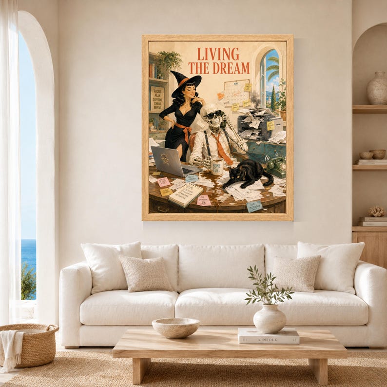 May include: A framed wall art print titled LIVING THE DREAM featuring a witch in a black dress and hat standing next to a skeleton wearing a tie and glasses at a cluttered desk with a laptop, printer, papers, and a black cat sitting on top.