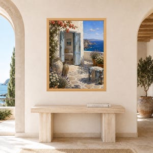 K&ouml;nnte beinhalten: Ein gerahmter Wandkunstdruck, der eine mediterrane K&uuml;stenszene mit einer offenen blauen T&uuml;r, einer Steinterrasse, Terrakottat&ouml;pfen, bl&uuml;henden Blumen und einem Blick auf das tiefblaue Meer unter klarem Himmel in einem hellen Holzrahmen zeigt.