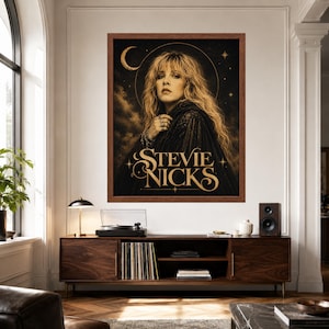 Puede incluir: Una impresi&oacute;n de arte de pared enmarcada que presenta un retrato de Stevie Nicks con cabello rubio largo, vistiendo una prenda de encaje oscuro. El fondo es negro con elementos celestiales dorados que incluyen una luna creciente y estrellas. El texto STEVIE NICKS est&aacute; en dorado.