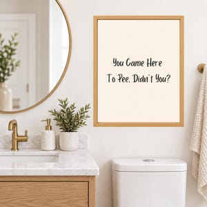 May include: A rectangular wall art print in a light wood frame featuring the black text "You Came Here To Pee, Didn't You?" on a cream-colored background. The print is displayed on a white wall above a white toilet in a bathroom setting.