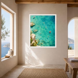 Puede incluir: Una impresi&oacute;n art&iacute;stica enmarcada que muestra una vista a&eacute;rea de agua de mar turquesa con acantilados rocosos, varios nadadores y un peque&ntilde;o bote. Un flotador circular de color naranja brillante es visible en el agua clara entre rocas.