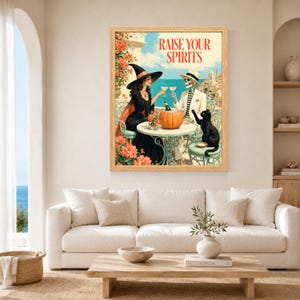 May include: A framed wall art print titled RAISE YOUR SPIRITS featuring a witch in a black dress and hat and a skeleton in a white suit sitting at a table with a pumpkin and a black cat, set against a coastal Mediterranean background.