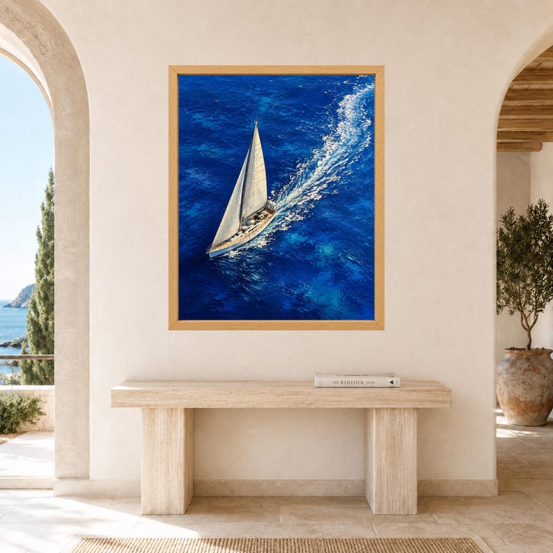 May include: A rectangular wall art print featuring an aerial view of a white sailboat navigating deep blue ocean waters. The vessel leaves a prominent white wake behind it, contrasting with the vibrant blue sea. The print is encased in a light wood frame.
