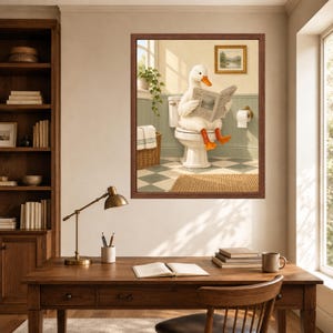 May include: A framed wall art print depicting a white duck with orange feet sitting on a white toilet in a bathroom, reading a newspaper. The bathroom features light green wainscoting, a checkered floor, a wicker basket, and a small framed landscape painting on the wall.
