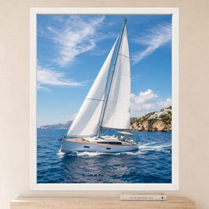 Puede incluir: Una impresi&oacute;n de arte mural enmarcada que muestra un velero blanco con las velas desplegadas navegando en aguas azul profundo bajo un cielo brillante con nubes tenues. La embarcaci&oacute;n tiene una cubierta de madera y un toldo beige.