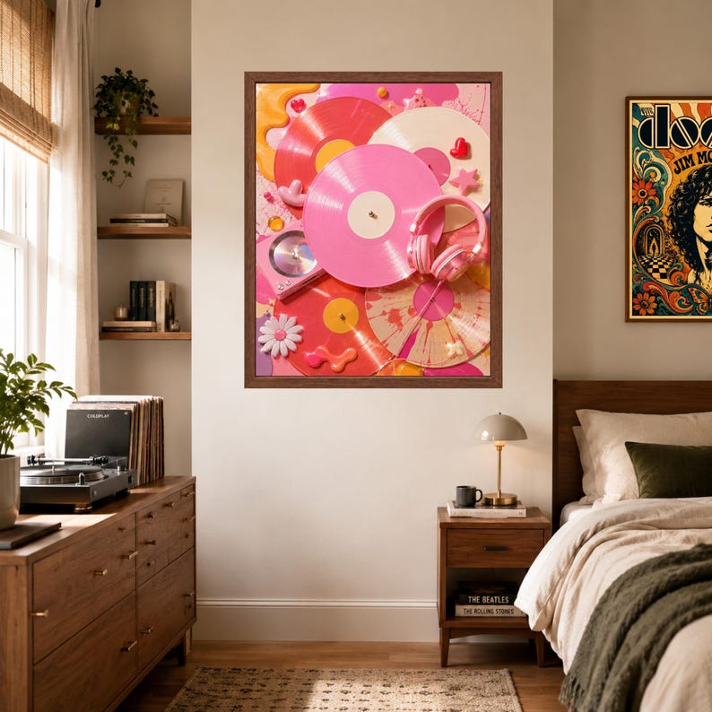 May include: A framed wall art print featuring a collage of vinyl records in shades of pink, white, and orange, accented with a pair of pink headphones, a small white daisy flower, and abstract shapes, all set against a vibrant pink background.