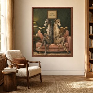 May include: A framed wall art print depicting two greyhounds sitting back-to-back on a pink sofa, each reading a book. Above them, a small sign reads "DOGS AT THE LIBRARY". The scene is set against a dark green wall with a lamp and books nearby.