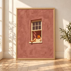 Framed dusty pink wall art showing a barefoot woman sitting in a small open window reading an orange book against a large textured blush rose facade.
