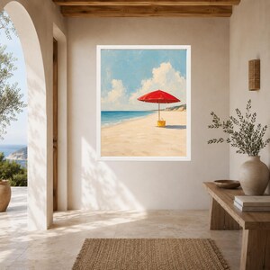 May include: A framed wall art print depicting a bright red beach umbrella and a yellow tote bag standing on a sandy beach under a blue sky with white clouds, overlooking the ocean with a distant coastline visible on the horizon.