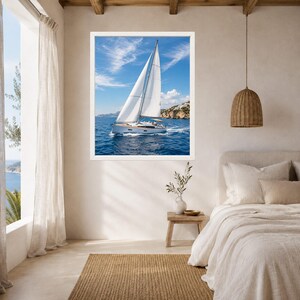 Puede incluir: Una impresi&oacute;n de arte mural enmarcada que muestra un velero blanco con las velas desplegadas navegando en aguas oce&aacute;nicas de color azul profundo bajo un cielo brillante con nubes tenues. La escena incluye una costa rocosa lejana en un marco blanco.