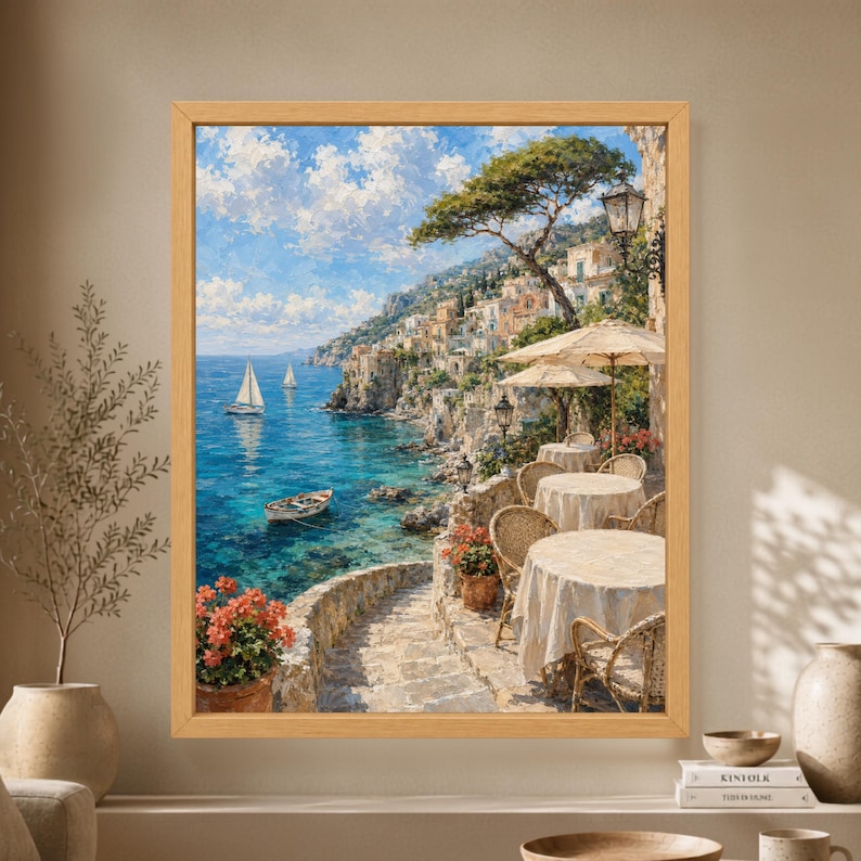 Framed Mediterranean terrace wall art showing a seaside café with linen-covered tables, woven chairs, turquoise water, sailboats and a sunlit Italian cliffside village.