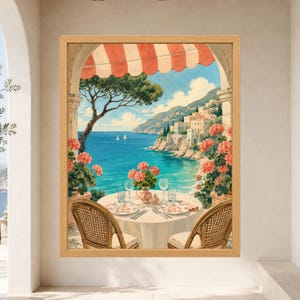 May include: A framed wall art print depicting a coastal scene viewed from a balcony with a red and white striped awning. The image shows a round table set for two with plates and glasses, flanked by two wicker chairs, overlooking a blue sea.