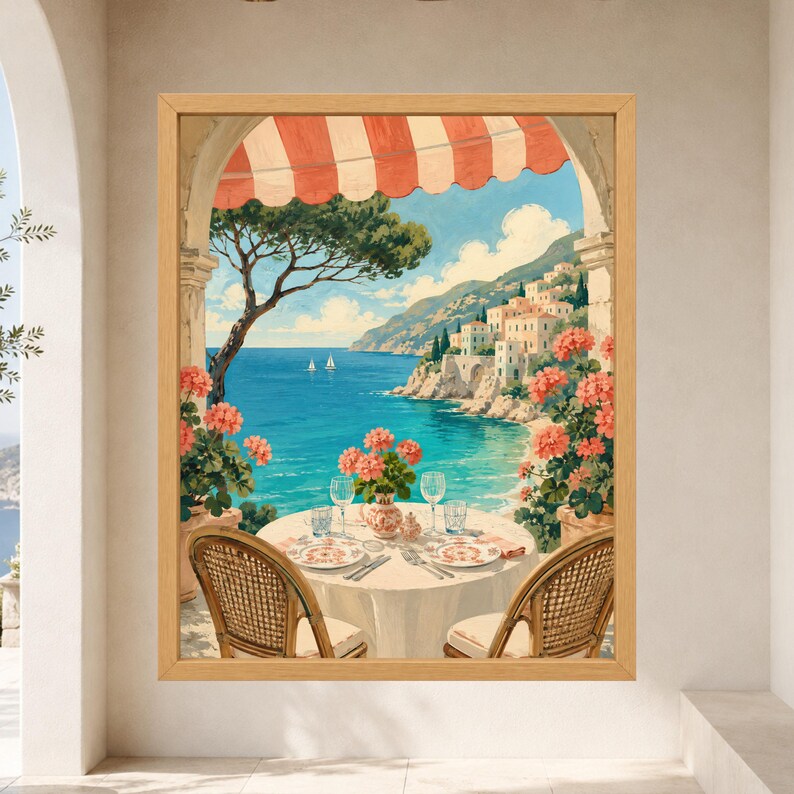 May include: A framed wall art print depicting a coastal scene viewed from a balcony with a red and white striped awning. The image shows a round table set for two with plates and glasses, flanked by two wicker chairs, overlooking a blue sea.