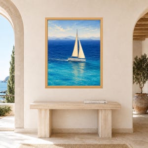 Peut inclure: Une impression d'art encadr&eacute;e repr&eacute;sentant un voilier blanc aux voiles beiges naviguant sur des eaux oc&eacute;aniques bleu vif sous un ciel clair, avec des montagnes lointaines &agrave; l'horizon. L'&oelig;uvre est pr&eacute;sent&eacute;e dans un cadre en bois clair.