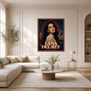 Puede incluir: Un p&oacute;ster de pared rectangular enmarcado que presenta el retrato de una mujer con cabello oscuro largo, sobre un cielo nocturno azul oscuro con una luna circular roja. El texto LANA DEL REY aparece en letras grandes color crema, con un motel.