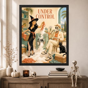 May include: A framed wall art print titled UNDER CONTROL featuring a witch in a black dress and hat doing laundry with a skeleton in a beige suit and hat sitting nearby drinking tea. A black cat sits on a wicker basket filled with folded towels.