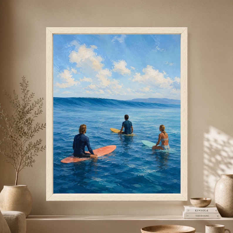 Framed surfing wall art showing three surfers sitting on colorful surfboards in clear blue ocean water while watching a long wave form beneath a bright cloud-filled sky.