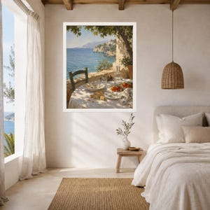 May include: A framed wall art print depicting a Mediterranean coastal scene with a table set for a meal on a terrace. The table features a white tablecloth, plates, bread, tomatoes, and a glass carafe, all under the shade of a tree by the sea.