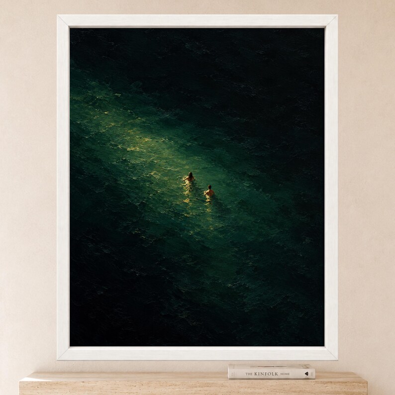 May include: A framed wall art print featuring a dark, deep green ocean scene with two figures swimming in a bright, narrow shaft of light that cuts through the center of the water. The frame is white and rectangular, surrounding the dark artwork.