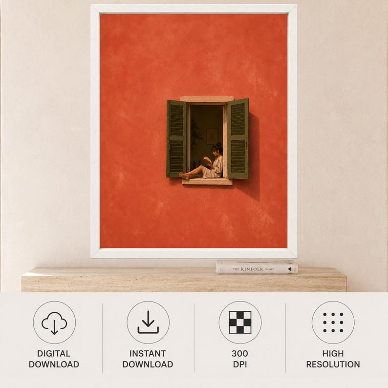 May include: A framed wall art print featuring a vibrant orange wall with an open window. Inside the window frame, a person sits while reading a book. The window has dark green shutters on both sides. The print is displayed in a white frame.