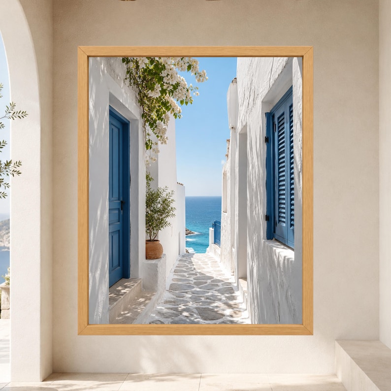 Framed Greek island coastal wall art showing a sunlit whitewashed stone alley with cobalt blue doors and shutters leading toward the deep blue Mediterranean sea beneath flowering bougainvillea.