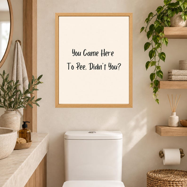 May include: A rectangular wall art print in a light wood frame featuring a cream-colored background with black text that reads: You Came Here To Pee, Didn't You? The print is displayed on a wall above a white toilet in a bathroom setting.
