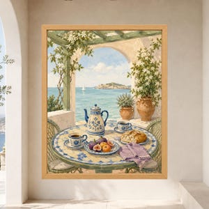 May include: A framed wall art print depicting a Mediterranean terrace scene with a tiled table holding a blue and white teapot, two cups of coffee, a plate of figs, and bread. The view shows a sea with a sailboat and distant hills under a blue sky.