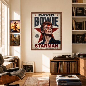 May include: A framed poster featuring a portrait of David Bowie with a red lightning bolt across his face, set against a large red star. The text reads DAVID BOWIE, STARMAN, and includes the lyrics THERE'S A STARMAN WAITING IN THE SKY and HE'D LIKE TO COME AND MEET US.