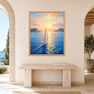 May include: A framed rectangular wall art print depicting a sailboat navigating deep blue waters during a golden sunset. The sky is filled with soft orange and yellow clouds, while the sun reflects brightly across the rippling sea surface.