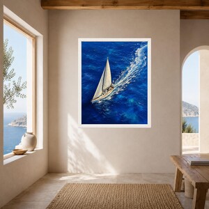 May include: A framed wall art print featuring an aerial view of a white sailboat gliding across deep blue ocean water. The vessel leaves a distinct white wake behind it, contrasting with the vibrant, textured shades of the sea surface.