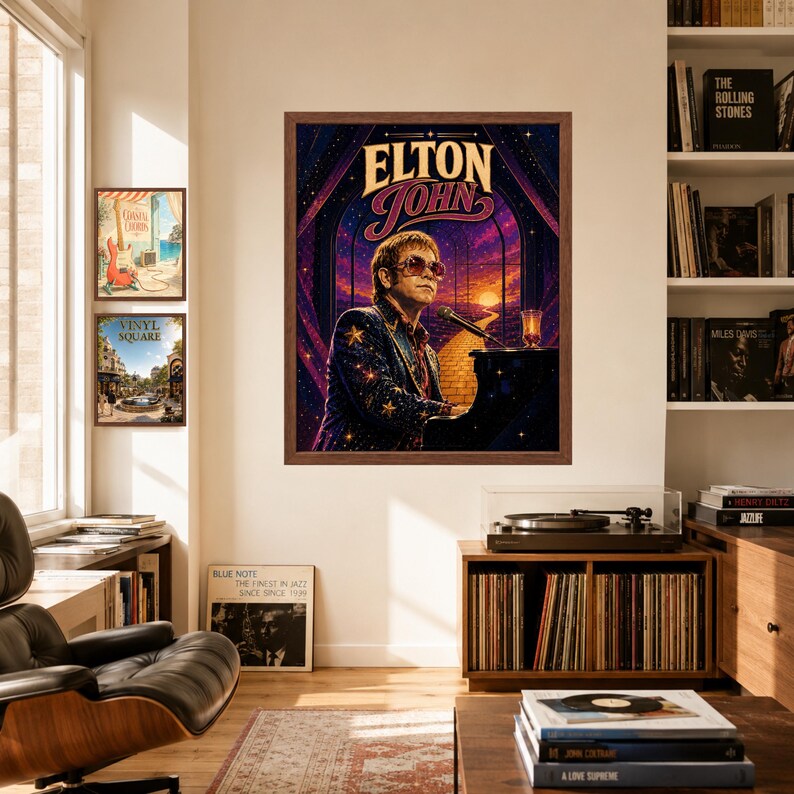 May include: A framed wall poster featuring an illustration of Elton John playing a grand piano. The artwork displays a starry night sky, a yellow brick road, and the text ELTON JOHN in a stylized font. The poster is mounted on a beige wall.