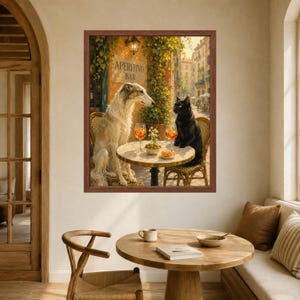 May include: A framed wall art print depicting a white Borzoi dog and a black cat sitting at a small round table outside an Aperitivo Bar. The table holds two orange cocktails and a small bowl of olives. The scene is set in a sunlit European street.