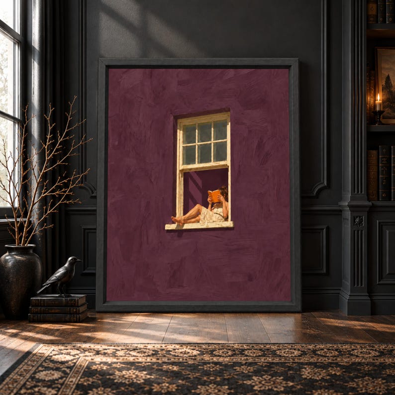 Framed burgundy wall art showing a woman sitting in an open window reading an orange book against a textured plum wall with warm cream trim.