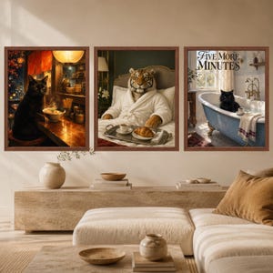 May include: A set of three framed wall art prints. The left print shows a black cat at a ramen bar. The centre print features a tiger in a white bathrobe in bed with a croissant. The right print depicts a black cat in a bathtub with the text Five More Minutes.