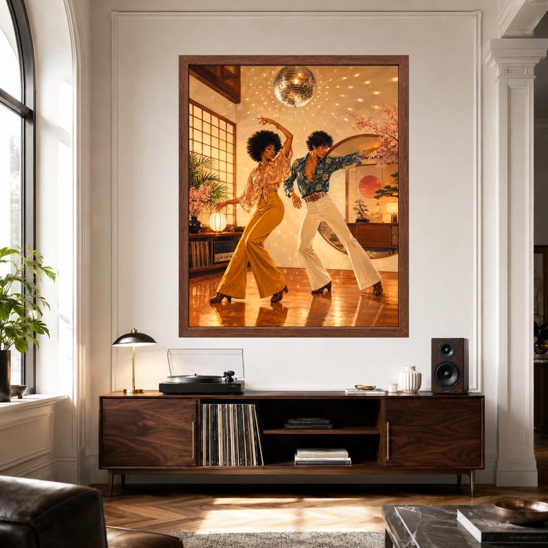 以下が含まれることがあります： ミラーボールのある部屋で踊る2人を描いた額入りアートプリント。1人は柄物のブラウスとマスタードイエローのフレアパンツを着用し、もう1人は青い花柄のシャツと白いフレアパンツを着用している様子が描かれています。