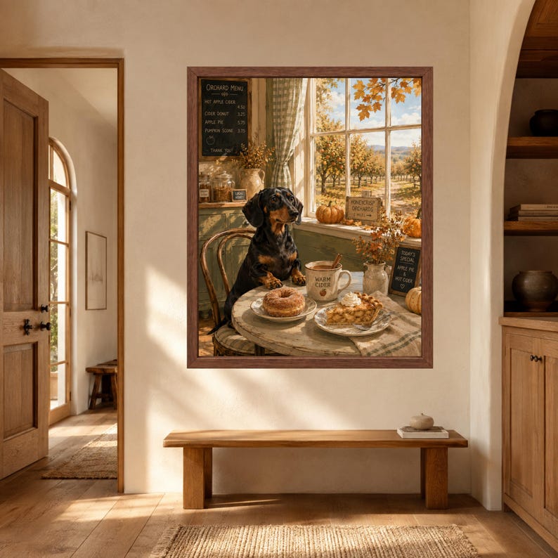 May include: A framed wall art print depicting a black and tan dachshund sitting at a round table in a rustic kitchen. The table holds a donut, a slice of pie, and a mug labelled Warm Cider. A window shows an orchard with autumn trees.