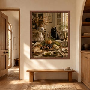 Op de afbeelding: Een ingelijste wandkunstprint met een grijs-witte whippet en een zwarte kat aan een eettafel, gedekt met een feestmaal van brood, druiven, vijgen, kaas, olijven en wijn, in een rustiek interieur met warme verlichting.