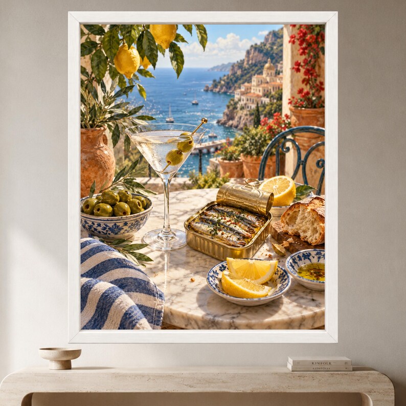 May include: A framed wall art print depicting a Mediterranean scene with a martini glass containing two olives, a tin of sardines, a bowl of green olives, lemon wedges, and bread on a marble table, set against a coastal cliffside view.