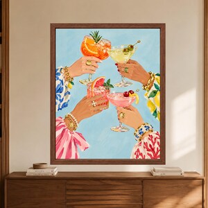 May include: A framed wall art print depicting four hands holding various cocktails against a light blue background. The drinks are garnished with orange slices, grapefruit, cherries, and olives. The hands wear gold bracelets and rings.