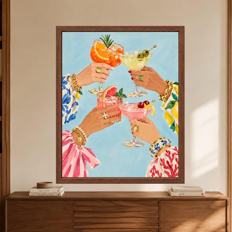 May include: A framed wall art print depicting four hands holding various cocktails against a light blue background. The drinks are garnished with orange slices, grapefruit, cherries, and olives. The hands wear gold bracelets and rings.