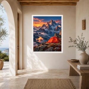 May include: A framed wall art print featuring a vibrant landscape scene of a bright orange tent perched on a rocky mountain ridge overlooking a lake, with snow-capped peaks in the background under a dramatic sunset sky with clouds.