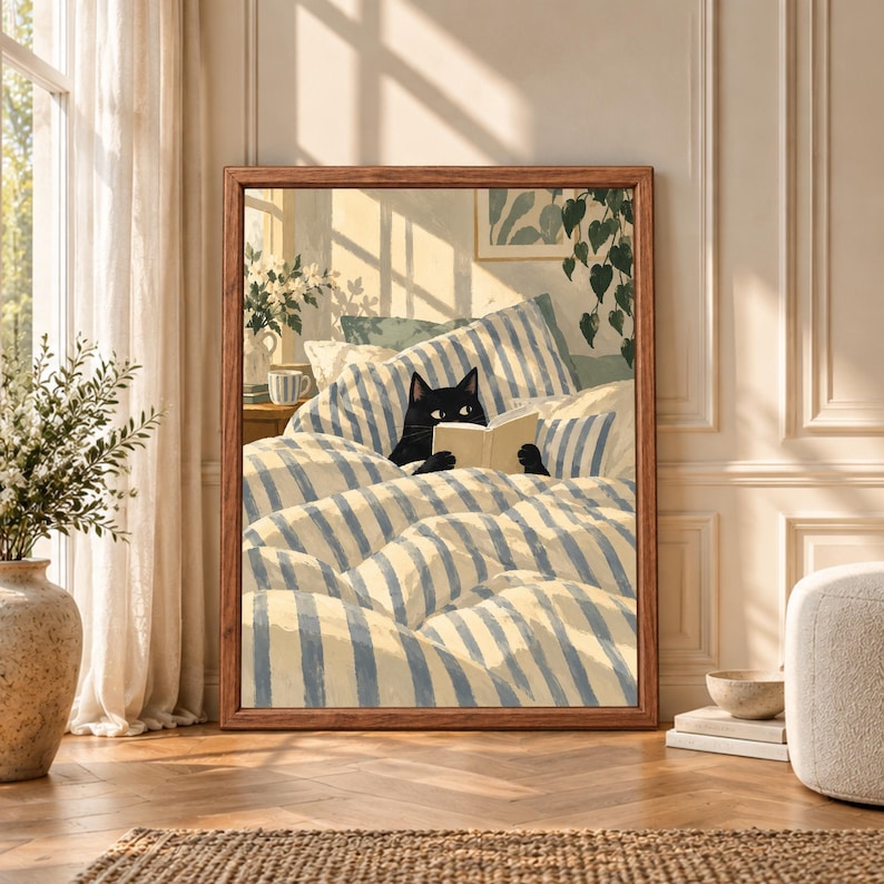 Framed black cat reading wall art showing a cat tucked into blue and cream striped bedding while holding an open book in a softly lit bedroom with plants and flowers.