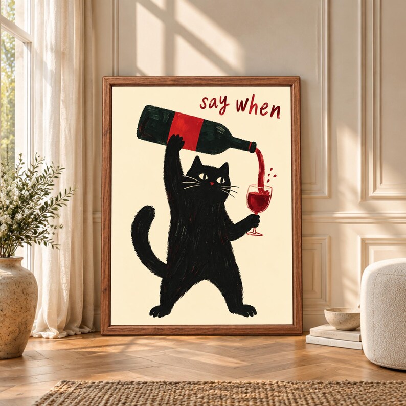 Framed funny black cat wine wall art showing a black cat pouring red wine from a large bottle into a glass beneath handwritten “say when” text on a warm cream background.