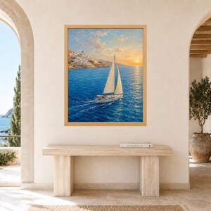 May include: A framed wall art print featuring a sailboat with white sails navigating deep blue waters at sunset. In the background, a coastal town with white buildings sits on a hillside under a soft, golden sky with scattered clouds.