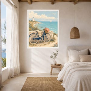 Op de afbeelding: Een ingelijste muurkunstprint met een kusttafereel met een blauwe fiets geparkeerd tegen een stenen muur. De fiets heeft een rieten mand aan de voorzijde met roze bloemen. Een vuurtoren staat op een grasachtige klif boven de blauwe oceaan.