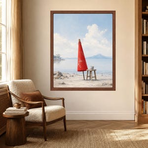 May include: A framed wall art print depicting a bright red paper umbrella standing upright on a sandy beach next to a small wooden stool. The background features a calm body of water, distant mountains, and a light blue sky with white clouds.