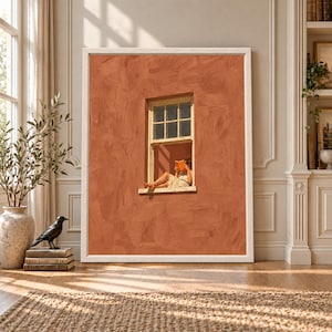 Framed terracotta wall art showing a woman sitting in an open window reading an orange book against a textured Mediterranean-style facade with warm sunlight.