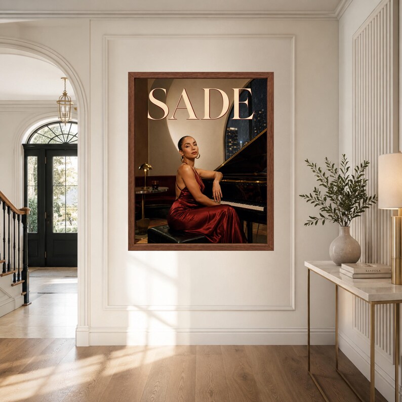 May include: A framed wall art print featuring a person in a dark red satin dress sitting at a black grand piano. The word SADE is printed in large, light-colored capital letters at the top. The scene is set in a dimly lit room with a warm glow.